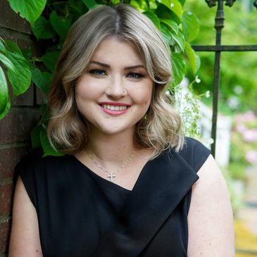 Smiling woman with blonde hair wearing a black dress outdoors.