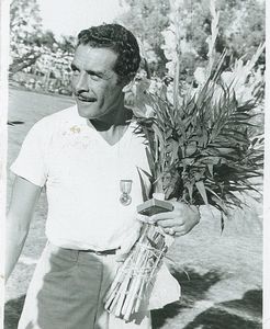 Man with a medal holding a bouquet of flowers at an outdoor event.