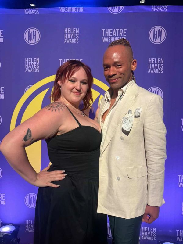 Two people posing at the Helen Hayes Awards with a purple backdrop.