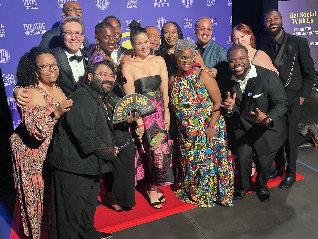 Group of people dressed formally posing on a red carpet at an awards event.