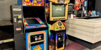 Two vintage arcade game machines, Ms. Pac-Man and Big Buck Hunter, side by side near a counter.
