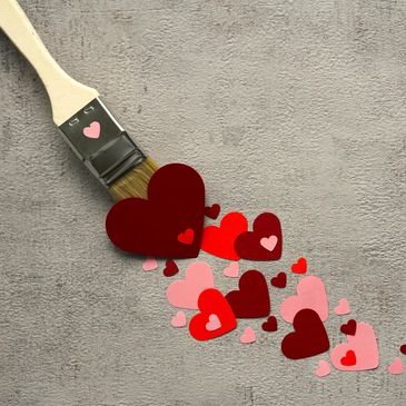 Paintbrush spreading colorful heart shapes on a gray surface.