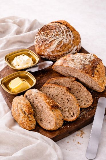 Sliced rustic bread with butter and cream on a wooden board.