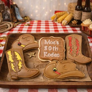 Western themed cookies on a wood tray, boot hat and words Moe's 80th Rodeo