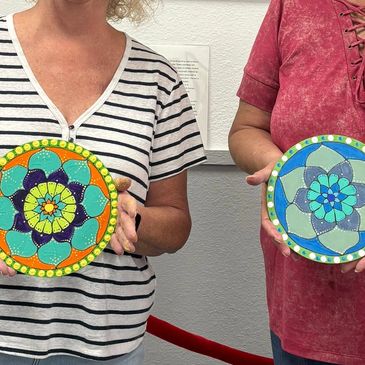 Two people holding colorful circular painted crafts.