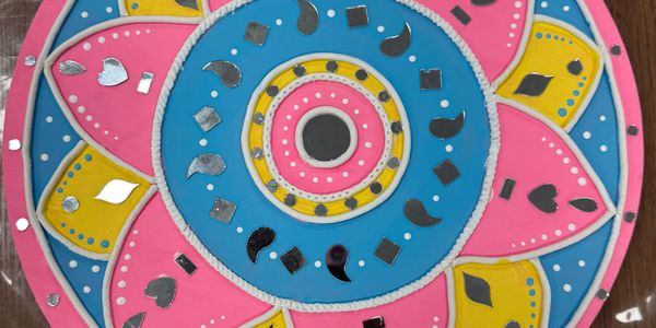 Colorful rangoli design with pink, blue, and yellow patterns and shiny silver embellishments.