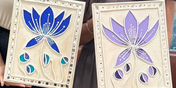Two framed floral artworks in blue and purple held by a person.