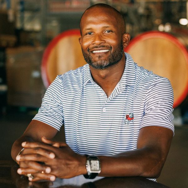 Smiling man in a striped polo shirt sitting at a table in a rustic setting.
