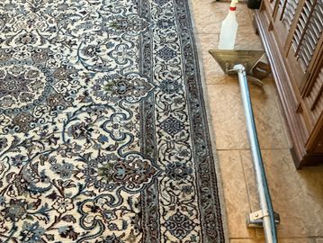 A patterned rug next to a tile floor with a cleaning tool and spray bottle.