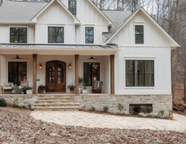 Modern farmhouse with a large porch surrounded by trees.