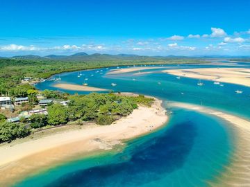 Aerial view of a winding river meeting the ocean with boats and sandy shores.
