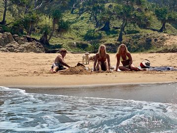 Three people and a dog enjoying a sunny beach day by the water.