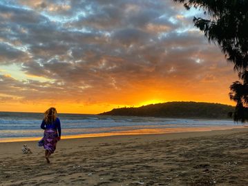 A person walking on a beach at sunset with vibrant orange sky.