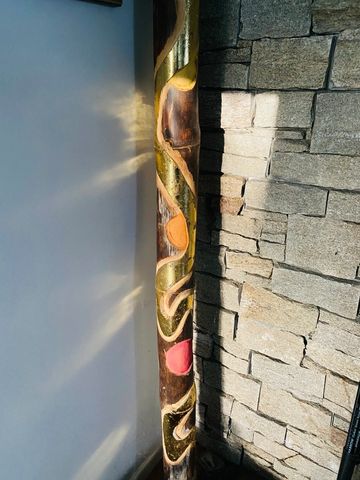 Decorative wooden pole with colorful patterns against stone wall and white background.