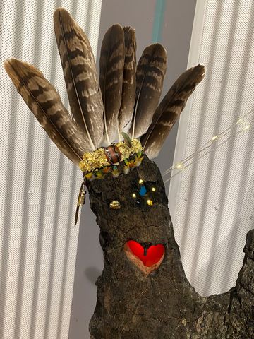 A tree stump decorated with feathers, lights, and a painted red heart.