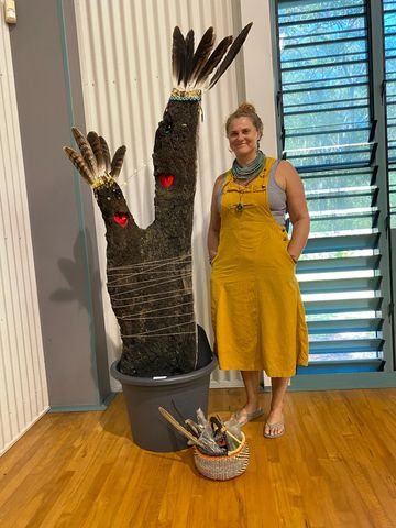Woman in yellow dress stands next to a decorated tree stump with feathers and hearts.