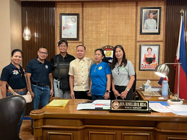 Group of six people standing behind an office desk with a nameplate of Hon. Roseller H. Rizal.