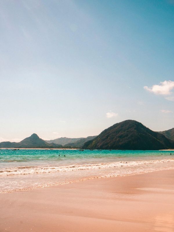 Serene beach with turquoise water and distant green hills under a clear blue sky.