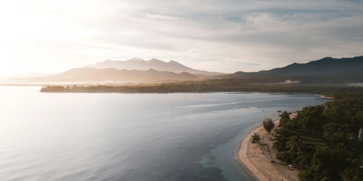 Calm coastal beach with mountains in the distance at sunset.
