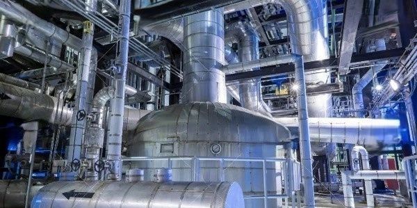 Interior of a large industrial plant with metal pipes and machinery.