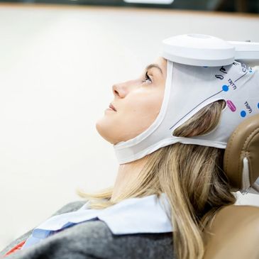 Woman undergoing a brain scan with a specialized headgear in a clinical setting.
