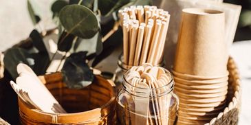 Eco-friendly disposable utensils and cups in a woven basket.