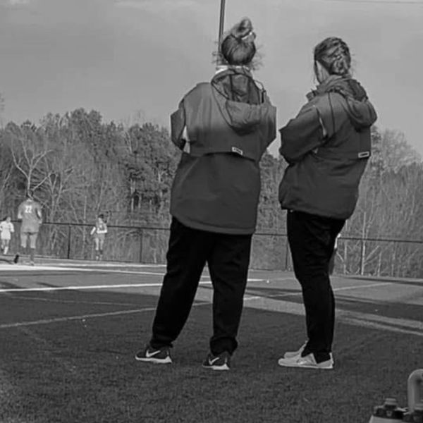 Two people standing on a sports field watching a game.