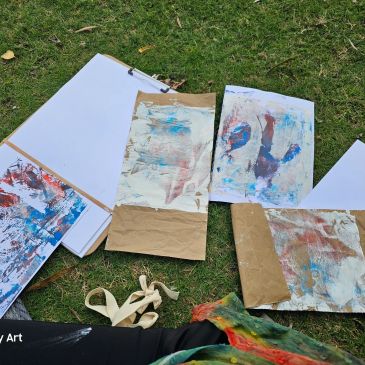 Abstract paintings and blank canvases laid on grass outdoors.