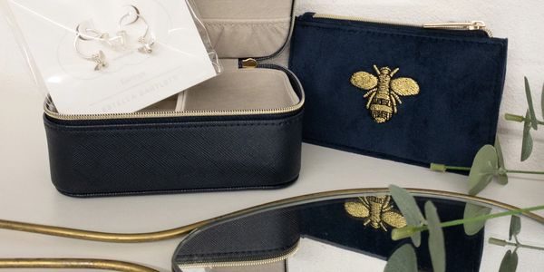 A hand held mirror next to a purse with embroidered bee detail and estella Bartlett jewellery case 