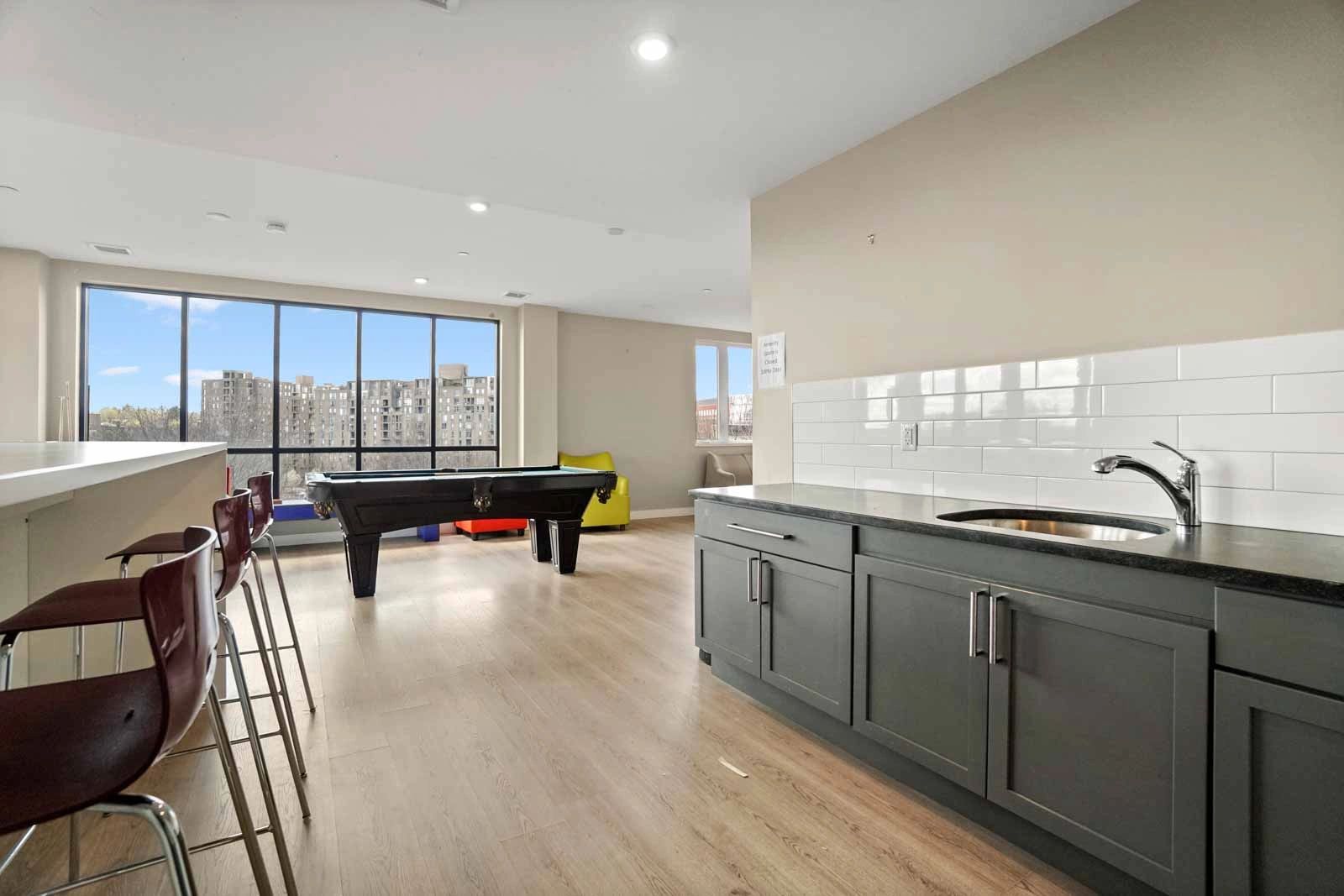 Modern room with a pool table, bar stools, and a kitchenette area.