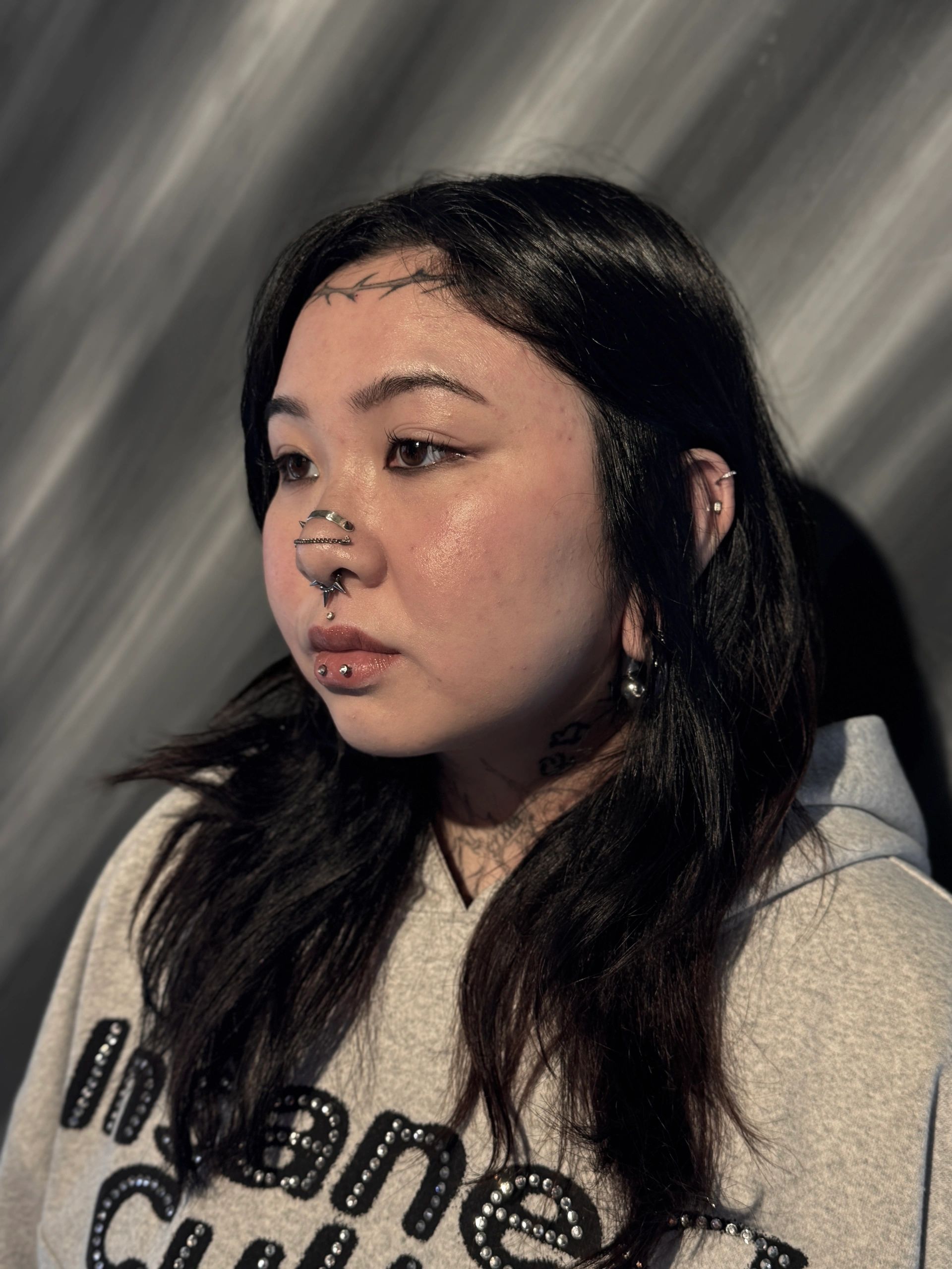 Black and white portrait of a woman with facial piercings and tattoos.