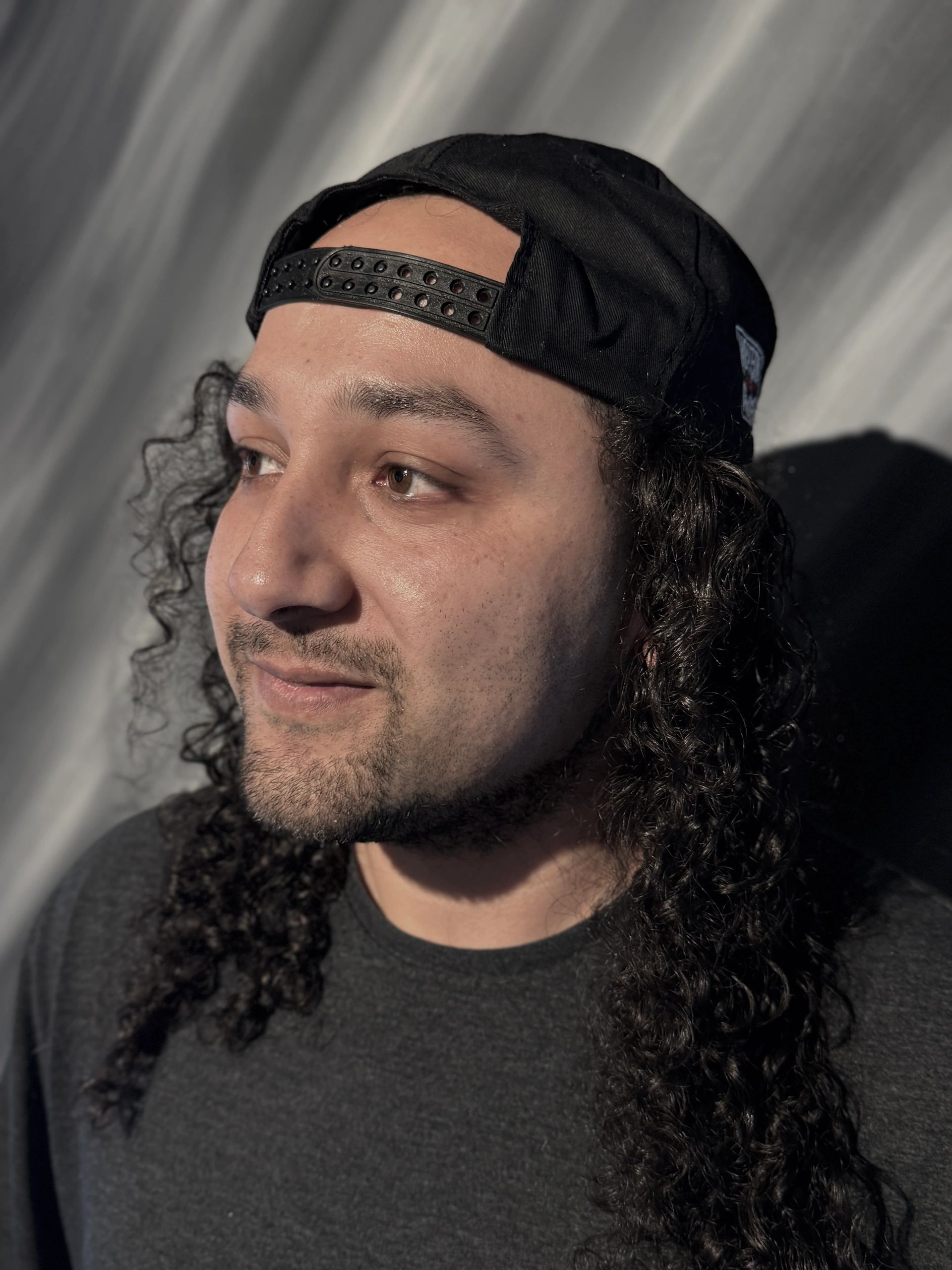 Man with curly hair wearing a backwards cap, looking sideways.