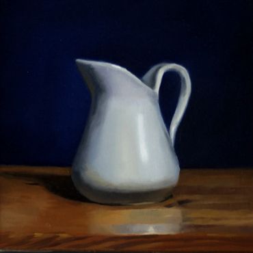 White ceramic pitcher on a wooden surface against a dark background.