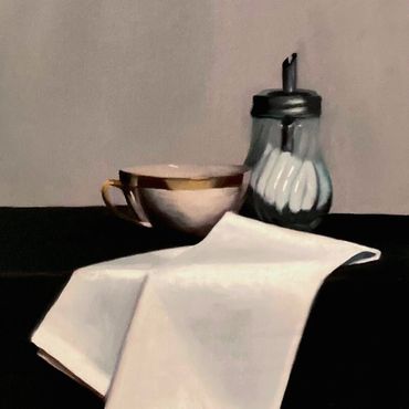 A cup, sugar dispenser, and white cloth on a dark table.