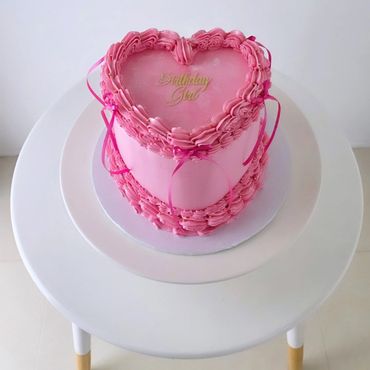 Heart-shaped pink birthday cake with decorative frosting.