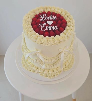 Elegant white cake with raspberries and names Lockie and Emma.