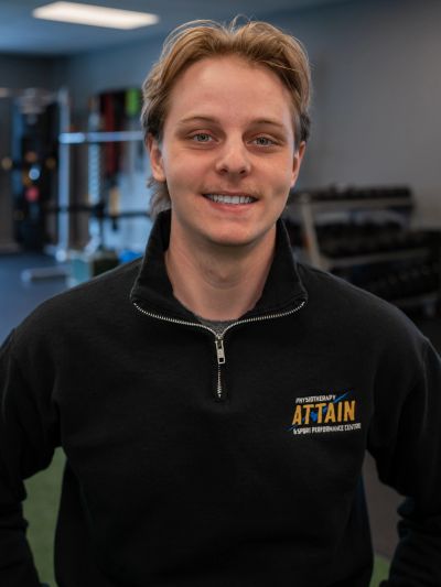 Young man in a black Attain sweatshirt smiling in a gym setting.