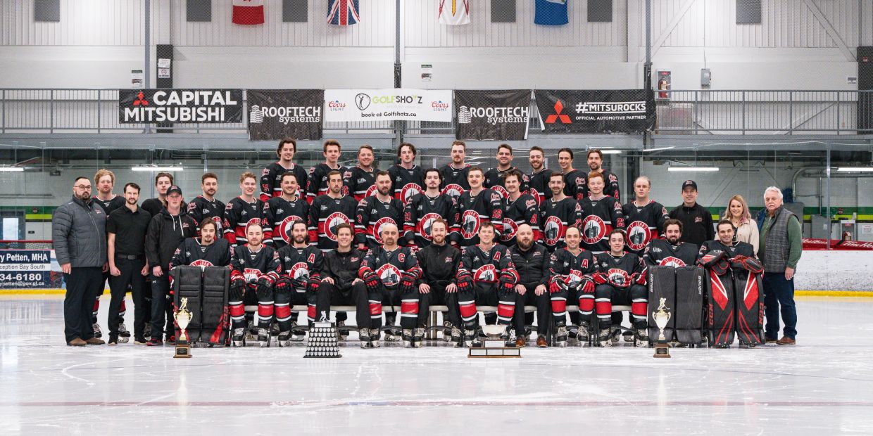 A hockey team posing on ice rink with trophies and banners.