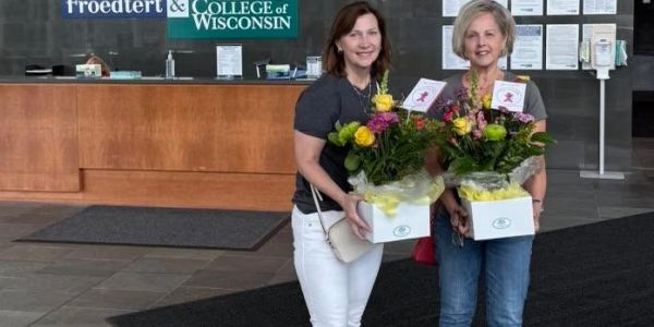 Two women holding flower arrangements inside a building.