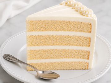 Slice of four-layer vanilla cake with white frosting.