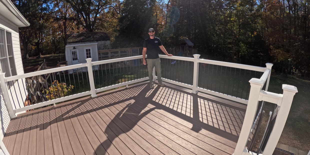 Man standing on a spacious deck with white railing on a sunny day.