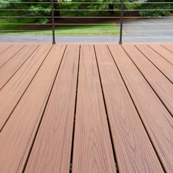 Close-up of a clean wooden deck with metal railing and greenery beyond.