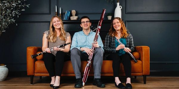 Three musicians sitting with wind instruments on an orange couch.