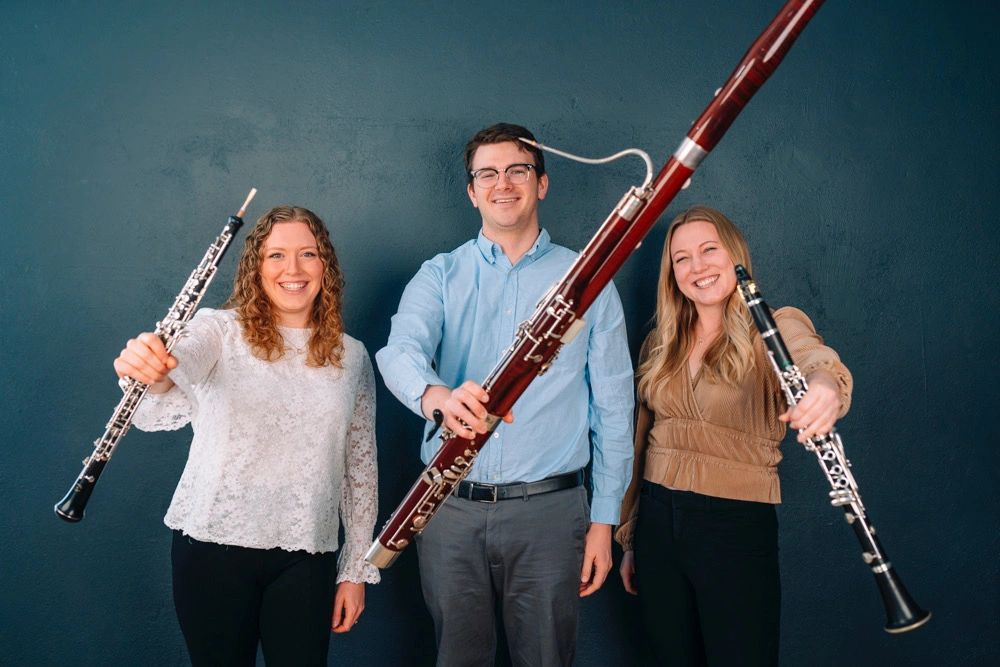 Three smiling musicians holding their woodwind instruments forward.