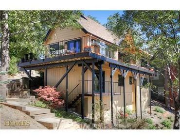 Two-story house with elevated deck surrounded by trees.
