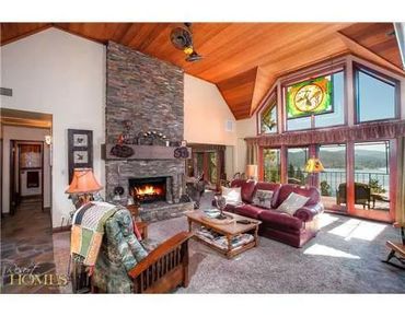 Cozy living room with stone fireplace and large windows overlooking a lake.