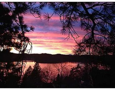 Vibrant sunset over a lake framed by silhouetted trees.