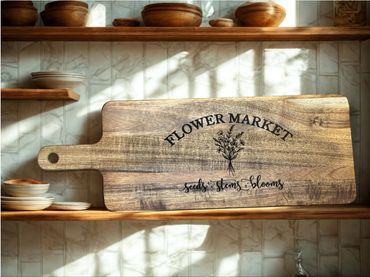 Rustic wooden cutting board with Flower Market design on a kitchen shelf.