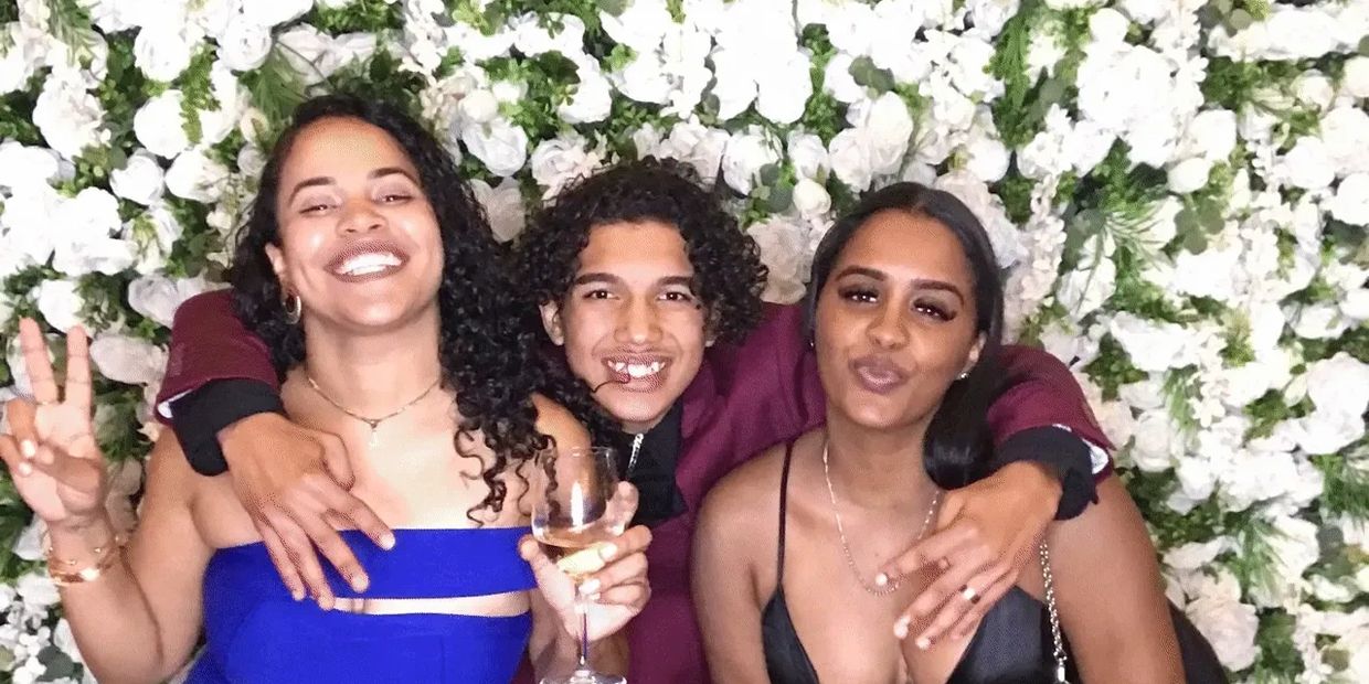 Three friends posing happily in front of a white floral backdrop at a party.