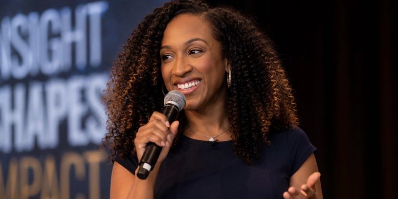 Woman with curly hair speaking confidently into a microphone.